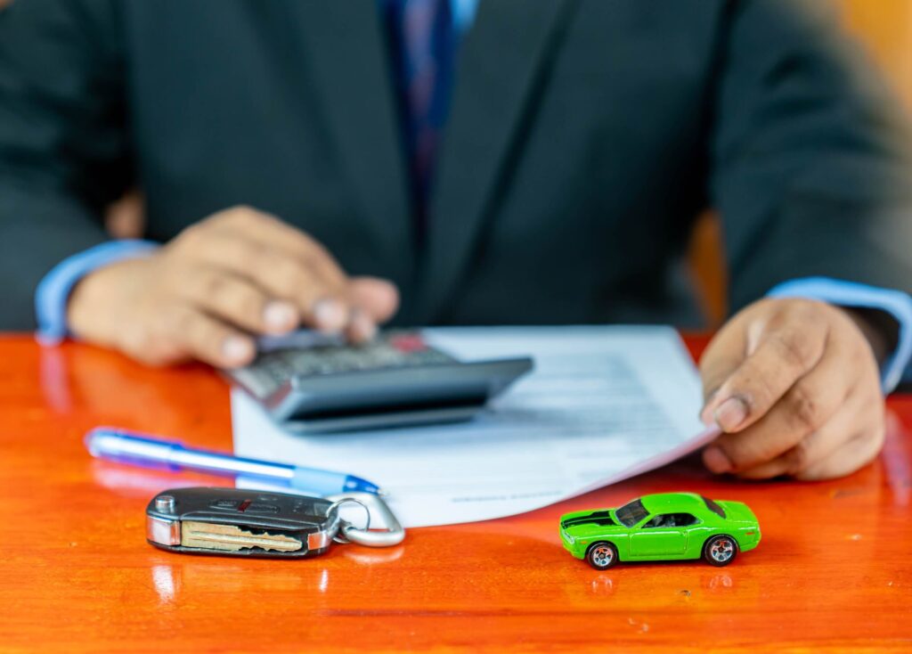 A person in a suit is working at a desk, using a calculator and calculating dealership fees.