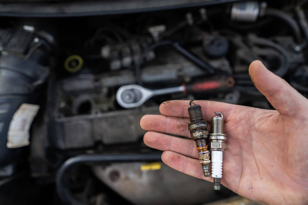 good and bad spark plug in the hands of a mechanic on the background of a car